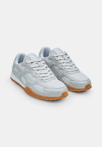 Chaussures de sport grises avec un mélange de daim et de matériaux en mesh. Elles présentent une semelle en caoutchouc gomme et sont équipées de lacets ronds dans une configuration standard.