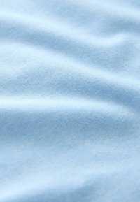 Tissu bleu clair doux avec une texture finement tricotée et des plis doux créant des ombres subtiles.