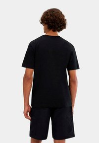 T-shirt nera in cotone con maniche corte, collo rotondo, design con cuciture piatte, indossata con pantaloncini cargo scuri, vista da dietro.