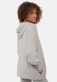 Sweat à capuche gris oversize avec une texture douce, dotée d'une capuche et de poches latérales. Le design présente des épaules tombantes et une coupe simple et décontractée.