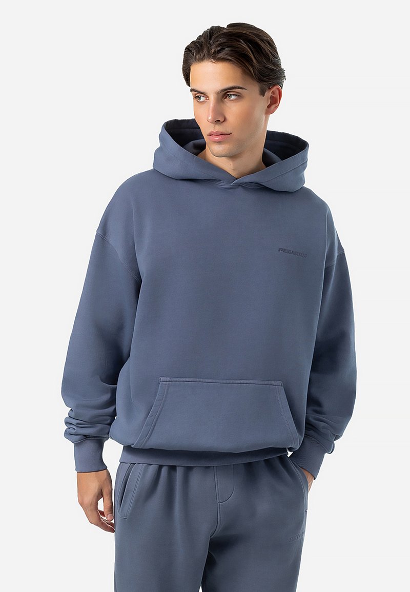 Hooded sweatshirt in muted blue, made of soft cotton. Features a front pocket and ribbed cuffs. Minimal branding on the chest.