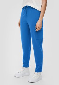 Modré, lehké joggers s elastickým pasem, šňůrkou, bočními kapsami a zúženým střihem nohavic. V kombinaci s bílými platformovými teniskami.