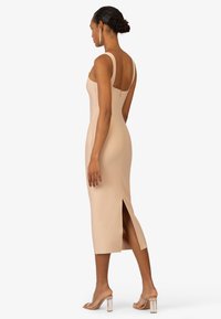 Vestito bodycon nudo con zip sul retro, spalline medie e spacco alto fino alla coscia; texture liscia e design aderente. Sandali con tacco trasparente.