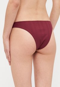 Burgundy bikini bottom with a ribbed texture, low-rise shape, and minimal coverage. Designed for comfort and flexibility.