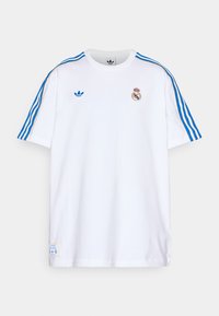 Hvit bomulls t-skjorte med blå og gull striper på skuldrene, Adidas-logo, Real Madrid-emblem, og en etikett på den nedre sømmen.
