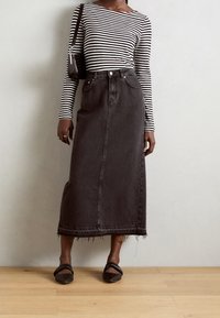 Schwarzer Denim-Maxi-Rock mit fransigem Saum, kombiniert mit einem langärmeligen Oberteil in Schwarz-Weiß-Streifen. Als Accessoire dient eine kleine schwarze Handtasche.