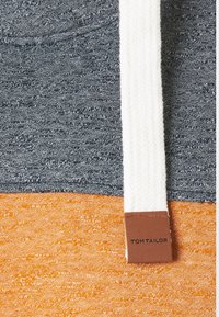 Sweat à capuche présentant un motif à blocs gris foncé et orange, en maille texturée, avec un cordon blanc au motif chevrons et une étiquette marron.