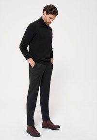 Czarny sweter z golfem, luźny krój; czarne spodnie z bocznymi kieszeniami; brązowe botki na sznurówki sięgające kostki o gładkim wykończeniu i gumowej podeszwie.