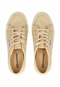 Zapatillas de lona beige con cordones planos, suelas de goma y marca Superga. Presentan una parte superior texturizada y detalles de costura reforzada.