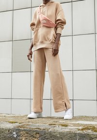 Beige oversized hoodie med en känguruficka, matchande vida sweatpants och en rosa crossbodyväska. Vita sneakers fulländar looken.