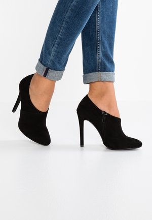 Sorte ruskinds stiletter med spids tå og lynlåslukning i siden, parret med oprullede blå denimjeans.