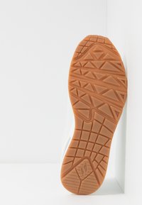 Semelle d'une sneaker avec un dessous en caoutchouc gomme, présentant un motif de grip texturé et le dessus blanc visible le long du bord.
