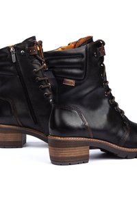 Svarta läderstövlar med snörning, vadderad krage, sidodragkedja och en brun träklack. Texturerad yta med subtila dekorationer.