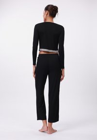 Black long-sleeve cropped top with a silver trim, paired with black loose-fitting pants, featuring an elastic waistband. Casual outfit displayed from behind.