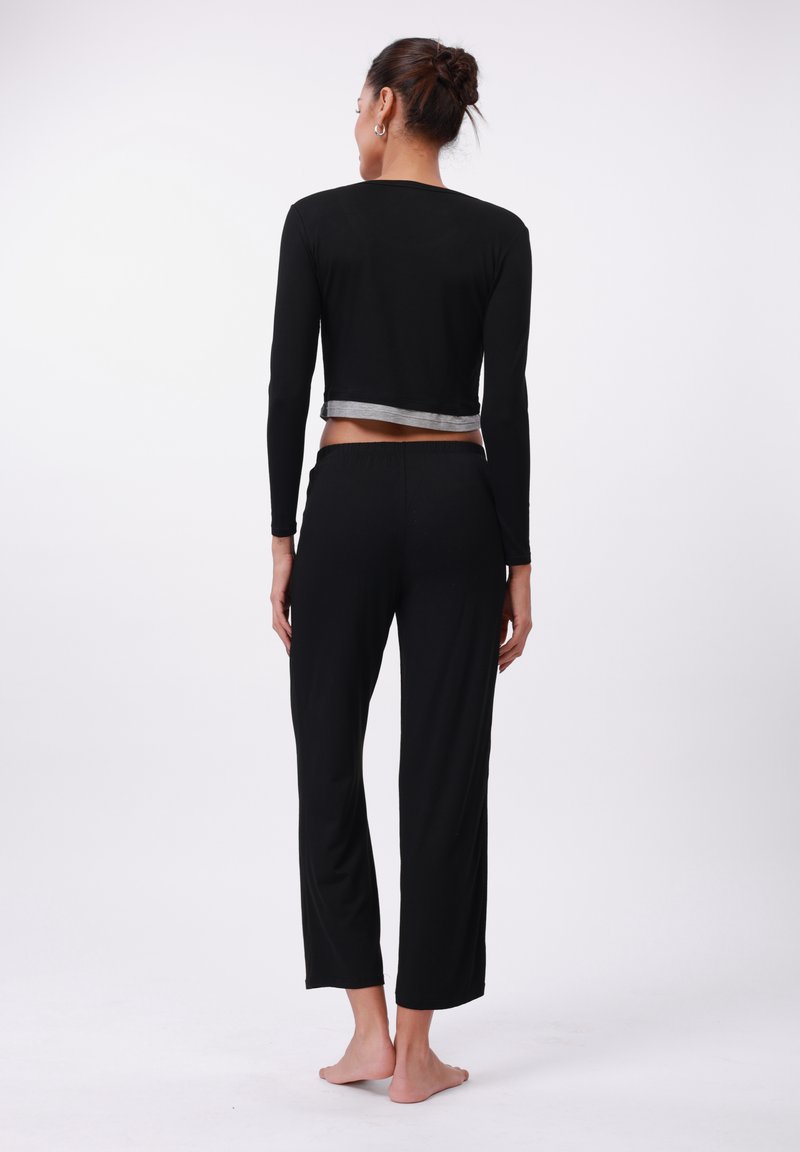 Black long-sleeve cropped top with a silver trim, paired with black loose-fitting pants, featuring an elastic waistband. Casual outfit displayed from behind.