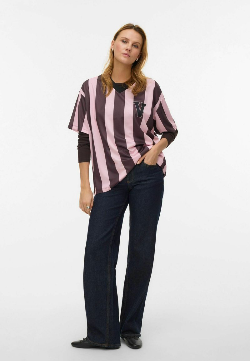 Dryžuota peraugusi rožinės ir tamsiai rudos spalvų marškinėliai su „V“ raidės ženklu kairėje krūtinės pusėje. Derinami su tamsiai platėjančiais džinsais ir juodais batais.