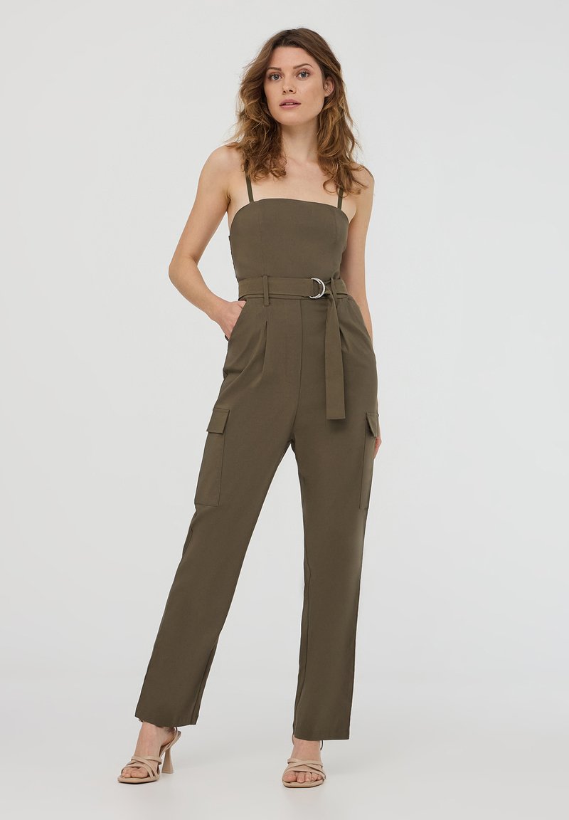 Tuta verde oliva con corpetto aderente, spalline sottili e vita con cintura. Presenta tasche laterali e gambe dritte, realizzato in tessuto leggero.