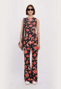 Black outfit with red hearts and floral patterns, sleeveless top and flared pants, paired with white shoes and a black strap bag.