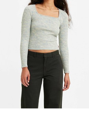 Kobieta w dopasowanym, długim rękawie, prążkowanym topie typu crop top z kwadratowym dekoltem oraz w czarnych, wysokim stanie spodniach.