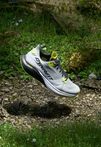 Ανοιχτό γκρι αθλητικό παπούτσι με μαύρες και νέον κίτρινες λεπτομέρειες, διαθέτοντας αναπνεύσιμο επάνω μέρος από διχτυωτό υλικό και ενισχυμένη σόλα σχεδιασμένη για τρέξιμο.