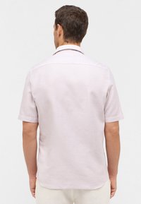 Licht lavendelkleurig T-shirt met korte mouwen van een textured stof. Kenmerken zijn een klassieke kraag, rugpand en een rechte zoom met zijsplitten.