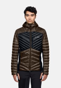 Giacca isolante con una combinazione di colori marrone e nero. Presenta una chiusura frontale con cerniera, una texture gonfia, un cappuccio e un motivo a zigzag sul petto.
