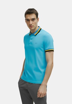 Polo blu chiaro con colletto a righe nere e gialle, tessuto morbido, taglio standard e un piccolo logo sul petto.