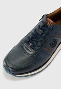 Sapatilha de couro azul-marinho com atacadores azuis, detalhes em castanho e um padrão texturizado. Apresenta uma etiqueta com o logótipo e uma sola de borracha branca e azul.