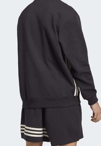 Svart sweatshirt och shorts-set; sweatshirten har rund halsringning och ribbat fåll. Shortsen har vita och beige randiga detaljer vid fållen.