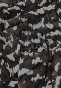Gros plan sur un tissu à motif camouflage noir, brun et blanc avec des coutures élastiques froncées et un bouton noir visible près du bas.