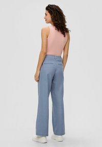 Leicht rosa Tanktop, kombiniert mit locker sitzenden hellblauen Hosen, die einen elastischen Bund und Seitentaschen haben. Weiße klobige Sneaker.