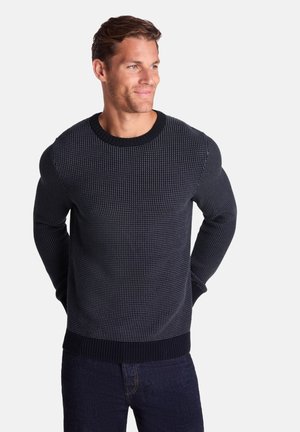 Crew-neck navy sweater with knit texture, featuring a ribbed hem and cuffs. Worn with dark jeans, displayed on a neutral background.