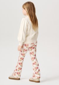 Kræmfarvet strikket sweater med diamantmønster, parret med flagrende bukser i blomstermønster med pink og grønne blomster.