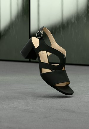 Zwarte sandalen met hoge hak en open neus, met een riemontwerp en een ronde zilveren gesp. Glad bovenmateriaal en blokhak.