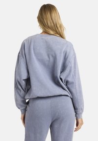 Sudadera de gran tamaño, de color azul claro, con una textura lavada, hombros caídos, puños de canalé y un escote redondo. Combinada con pantalones a juego.