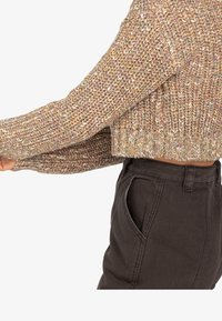 Pull court en maille tricotée avec un fil multicolore et une finition texturée. Doté de manches longues et d'un large ourlet côtelé. Associé à un pantalon foncé.