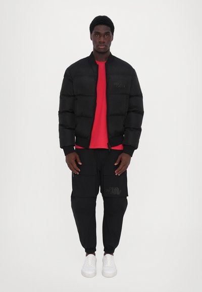 Black puffer jacket with a ribbed collar, red t-shirt underneath, black cargo pants with pockets, and white sneakers. Simple, athletic fit.