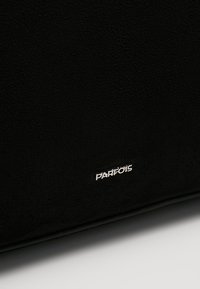 Černá texturovaná tkanina s malou stříbrnou kovovou destičkou "PARFOIS" poblíž spodního okraje na bílém pozadí.