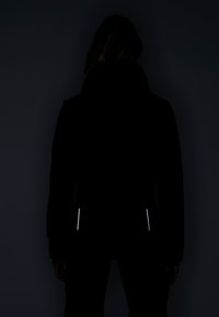 Schwarze Kapuzenjacke mit reflektierenden Seitenelementen; glatte Textur, körperbetonte Form und nahtloses Design, vor einem dunklen Hintergrund gezeigt.