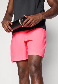 Férfi sportshort, élénk rózsaszín színben, könnyű anyagból készült; elasztikus derékrésszel és New Balance logóval az oldalon.