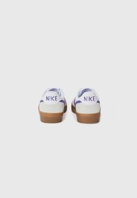 Valged Nike tennised, millel on lillad aktsendid, sametist ja nahast materjalid, kummist tallad ning kahekordne logo detail kannal.
