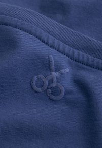 Marineblauwe stof met een gladde textuur, voorzien van een geborduurd schaarlogo in een iets donkere tint. Eenvoudig stikselontwerp langs de rand.