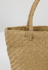 Panier en fibres naturelles tressées avec une poignée solide en tresse et un motif en zigzag sur le côté, posé sur un fond uni.