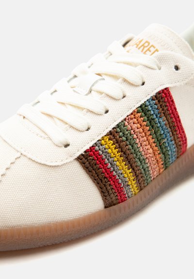 Baskets blanches avec lacets crème et une bande latérale en tissu tissé multicolore aux tons rouges, jaunes, verts, bleus et bruns.