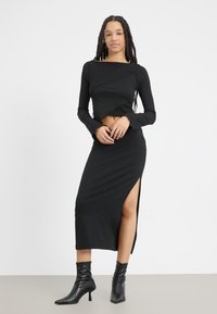 Black long-sleeved cropped top with textured design, paired with a fitted black maxi skirt featuring a side slit, worn with pointed ankle boots.