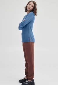 Ljusblå tröja med långa ärmar och sidofickor, parat med bruna byxor med elastiskt midjeband. Svarta platåskor med gyllene detaljer.