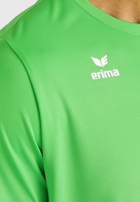 Groene sportieve shirt gemaakt van textuurstof, met een ronde halslijn en een klein wit "Erima" logo op de borst.