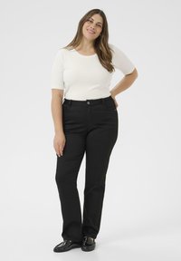 Schwarze knöchellange Hose mit klassischem Schnitt, hoher Taille und Fünf-Taschen-Design, kombiniert mit einem kurzärmligen weißen Oberteil.