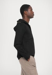 Black zip-up hoodie with a hood and gold zipper detail, made of soft material, featuring angled front pockets and a relaxed fit.