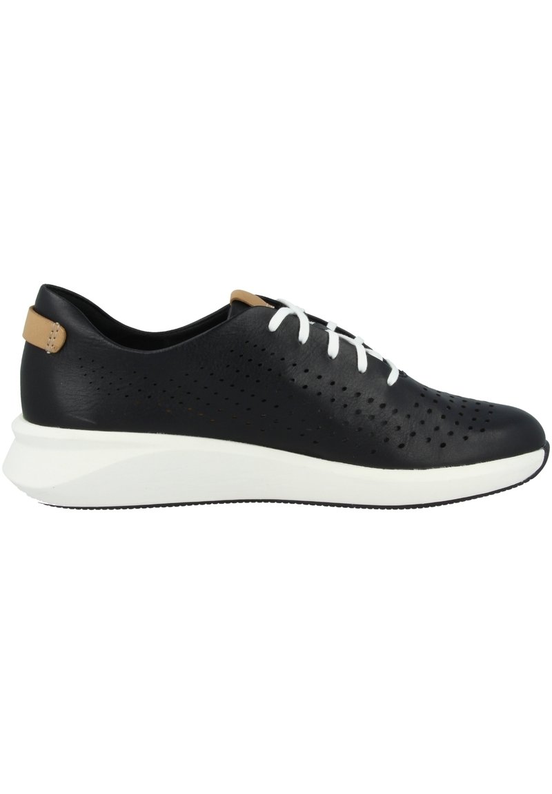 Baskets noires perforées avec des lacets blancs et un onglet de talon contrastant en tan, présentant une texture lisse et une semelle blanche légère.